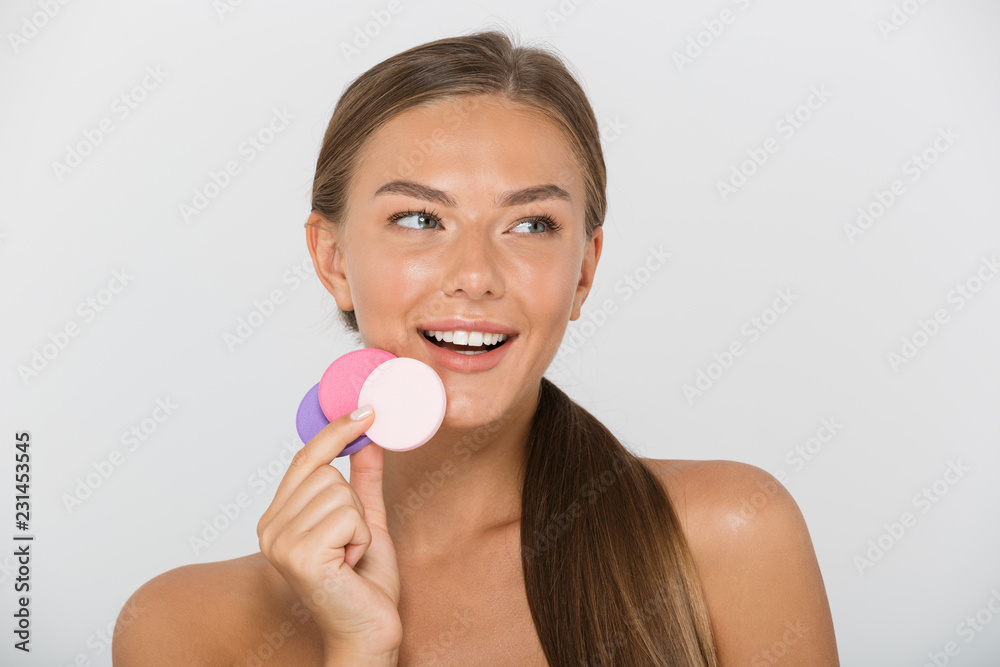 Beauty portrait of brunette shirtless woman with long brown hair smiling and holding colorful cosmetic pads, isolated over white background Beauty portrait of brunette shirtless woman with long brown hair smiling and holding colorful cosmetic pads, isolated over white background