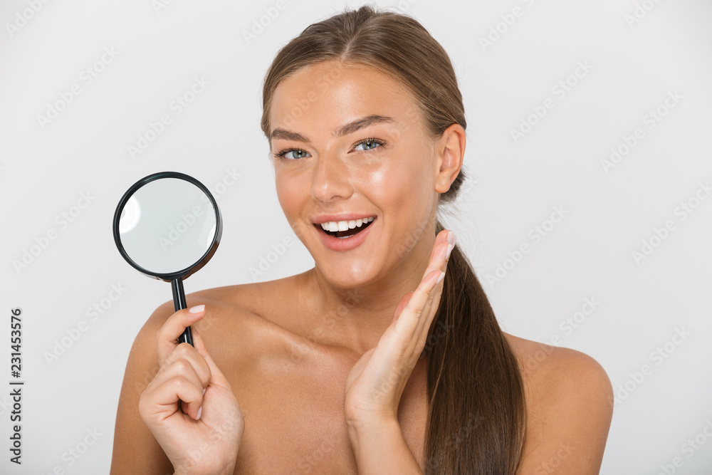 Beauty portrait of happy shirtless woman with long brown hair holding magnifying glass, isolated over white background Beauty portrait of happy shirtless woman with long brown hair holding magnifying glass, isolated over white background