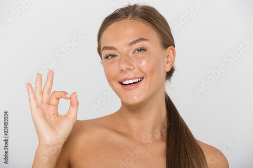 Beauty portrait of pretty shirtless woman with long brown hair smiling and showing ok sign, isolated over white background