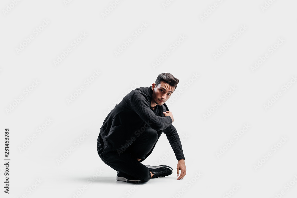 Dark-haired stylish dancer dressed in a stylish black clothes is sitting on the floor