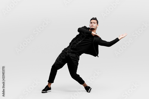 Dark-haired stylish young man wearing a black sweatshirt and black pants makes stylized movements of street dances