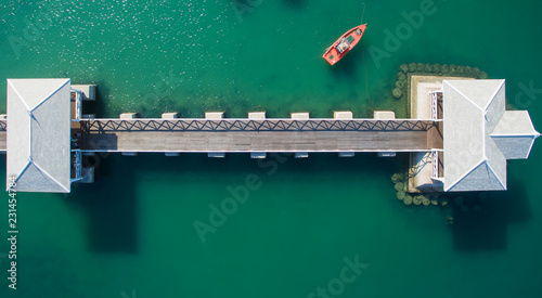 Aerial view of natural clear blue sea with sea floating bridge and boat. Aerial: Shoreline with fishing boats and long tail taxi boats parking along the sand beach.