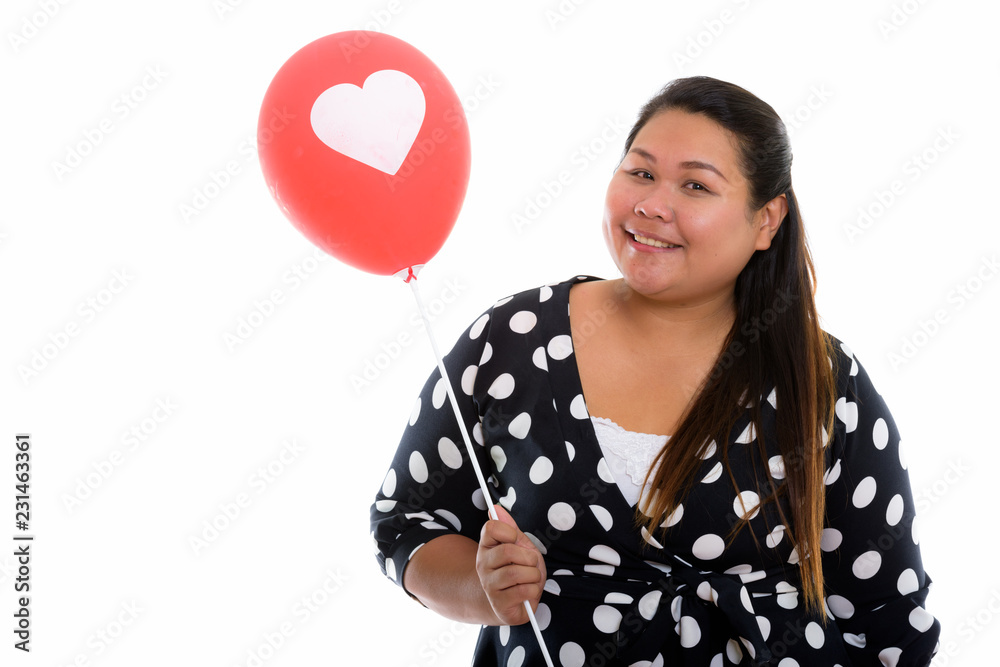 Studio shot of young happy fat Asian woman smiling while holding