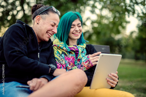 Two young girls sitting in the park, having fun, taking photos and enjoying time spent together. Couple concept.