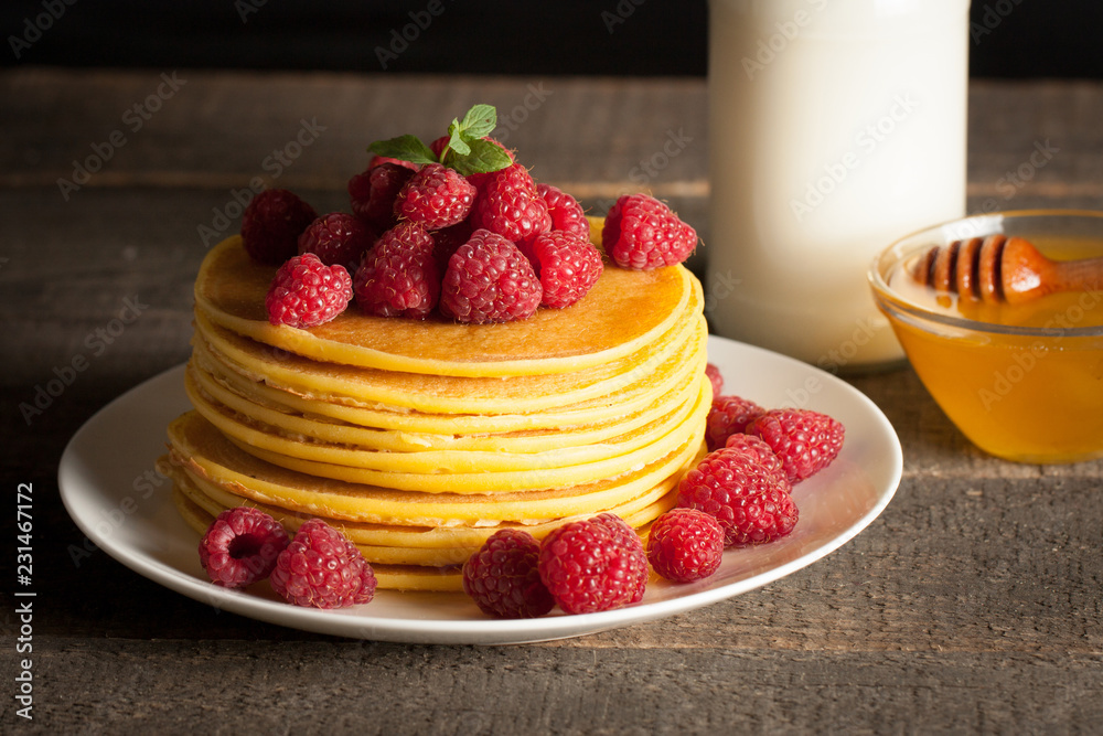 Tasty pancakes with blackberries, banana, raspberries, eggs, honey and maple syrup on wooden background. Morning breakfast concept.