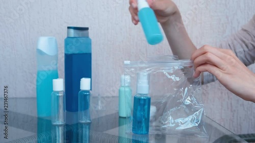 Women's hands put a road set of cosmetics with bottles and jars in a zip plastic pouch. Close-up jars.