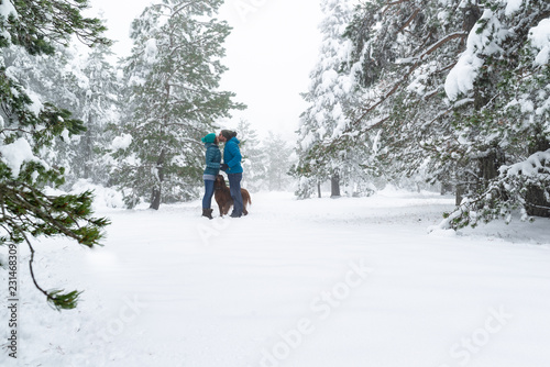  Pareja de enamorados besándose y abrazando a su perro en un hermoso bosque nevado. Feliz fin de semana al aire libre.