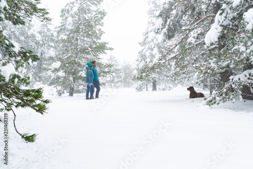 Mujer, hombre y su perro disfrutando de un día en un bosque de pinos nevados. Feliz fin de semana de invierno.