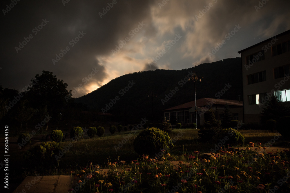 Mountain night landscape of building at forest at night with moon or vintage country house at night with clouds and stars. Summer night.