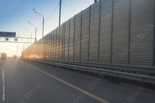 Morning traffic on a highway with lighting poles and metal rails of the safety barrier
