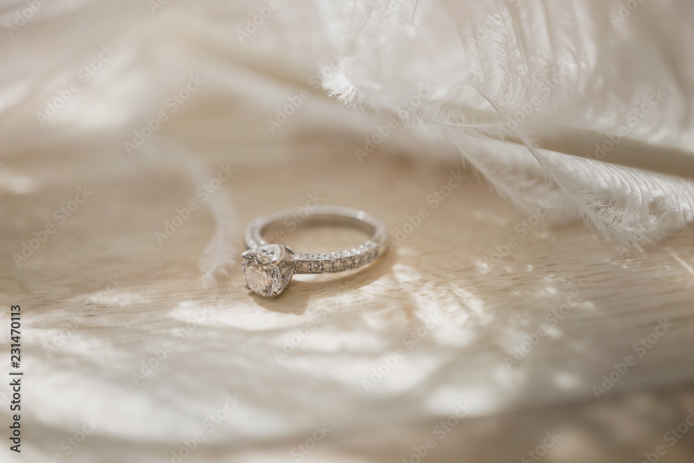 Close up of an elegant diamond ring and feather on wood background. soft and selective focus. Love and wedding concept. Close up of an elegant diamond ring and feather on wood background. soft and selective focus. Love and wedding concept.