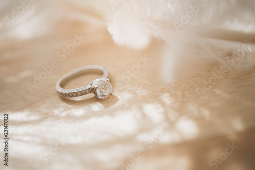 Close up of an elegant diamond ring and feather on wood background. soft and selective focus. Love and wedding concept.