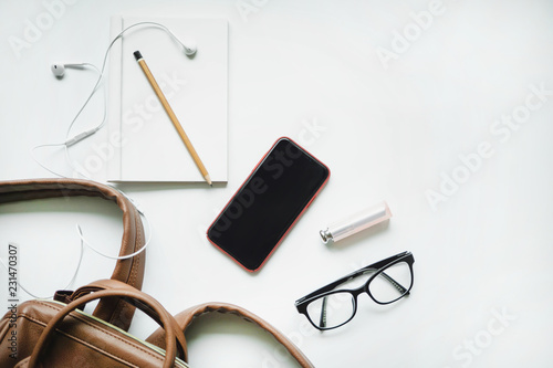 BANGKOK,THAILAND Oct 10,2018 : Top view of woman black bag open out with accessories Apple Iphone X with notebook, pen, glasses, earphone on white background.