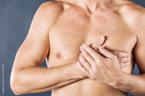 Man suffering from chest pain, having heart attack or painful cramps, pressing on chest with painful expression on blue backgound. Severe heartache