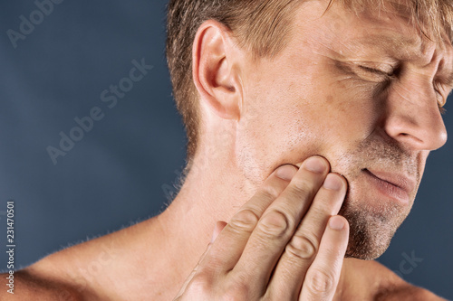 Sad depressed man in pain holding his cheek. Portrait of a man on blue background. emotion facial expression. feelings and people reaction. Toothache