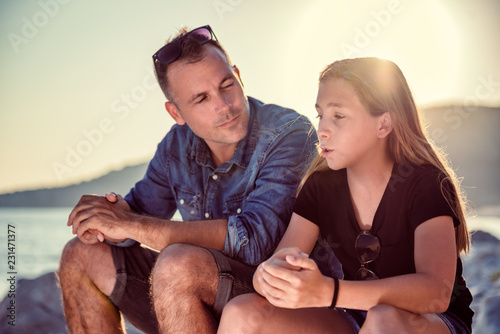 Father and daughter sitting on a rocky beach and talking