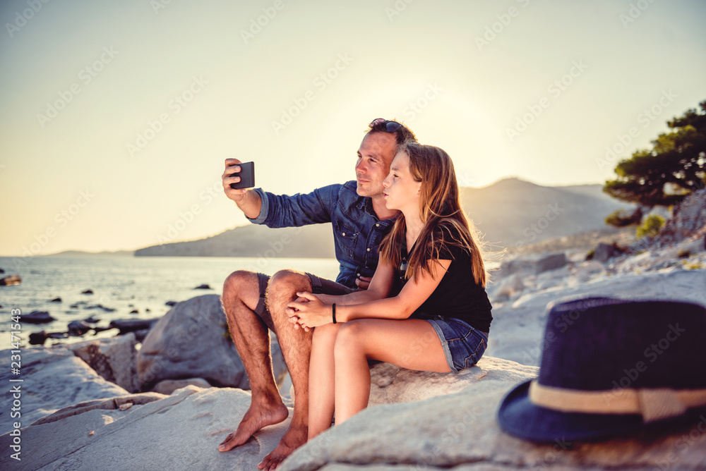 Father and daughter sitting on a rocky beach and taking selfie Father and daughter sitting on a rocky beach and taking selfie
