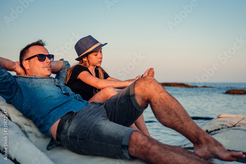 Father and daughter lying down on rocks at beach