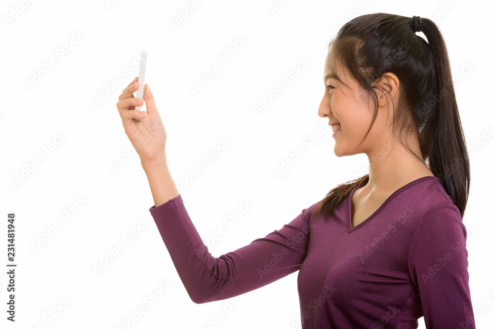 Profile view of young happy Asian teenage girl smiling while tak Profile view of young happy Asian teenage girl smiling while tak