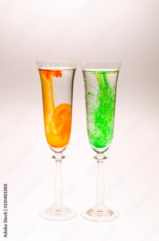 The effect of water smoke using an orange and green food coloring in two glasses for champagne on a white background.