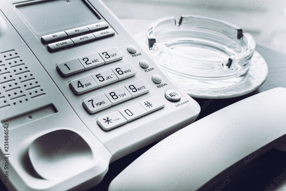 White phone with the picked up phone near glass ashtray for smoking on wooden table. White phone with the picked up phone near glass ashtray for smoking on wooden table.