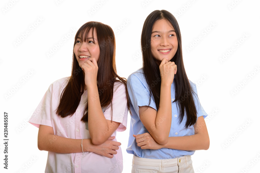 Two young happy Asian teenage girls smiling and thinking togethe Two young happy Asian teenage girls smiling and thinking togethe