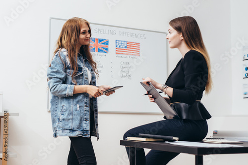 Two female students talking in classroom. College, English language school.