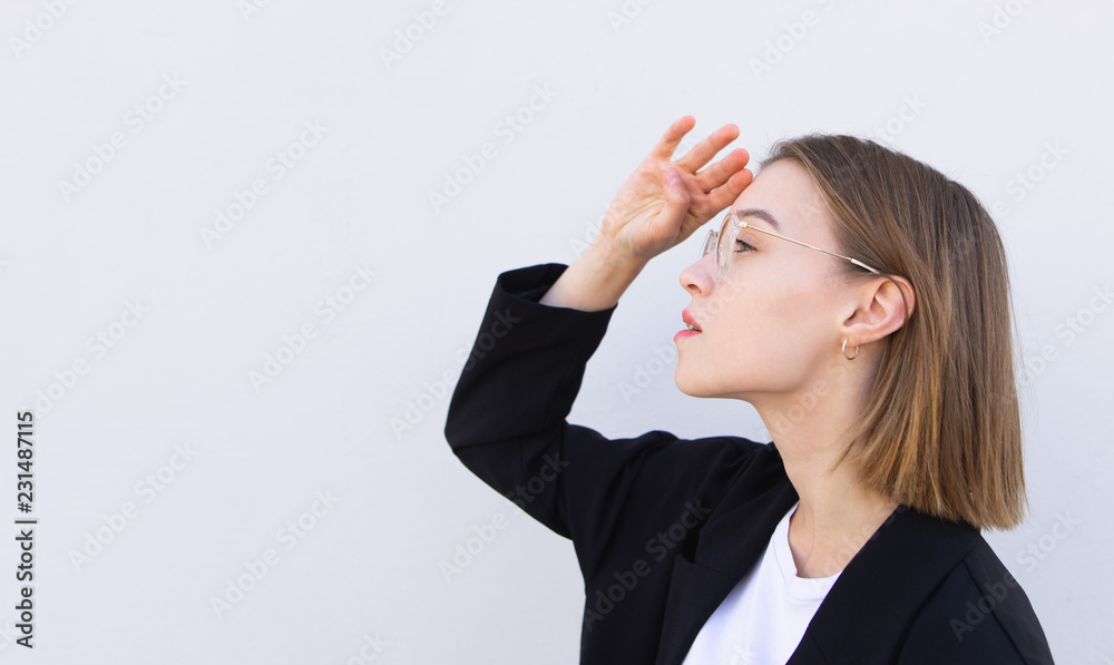 Young attractive business woman in glasses and a black jacket looks sideways on a white background. Look at the place for the text Young attractive business woman in glasses and a black jacket looks sideways on a white background. Look at the place for the text