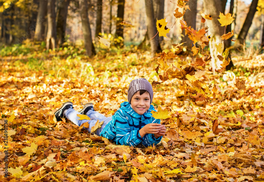 Child boy in autumn park with falling leaves. He lies on the yellow leaves. Child boy in autumn park with falling leaves. He lies on the yellow leaves.