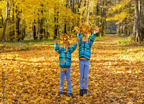 Twin boys in the park under falling maple leaves. Autumn.