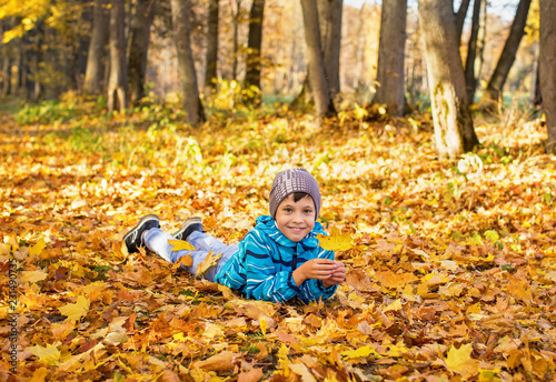 Child boy in autumn park with foliage. He lies on the yellow leaves.