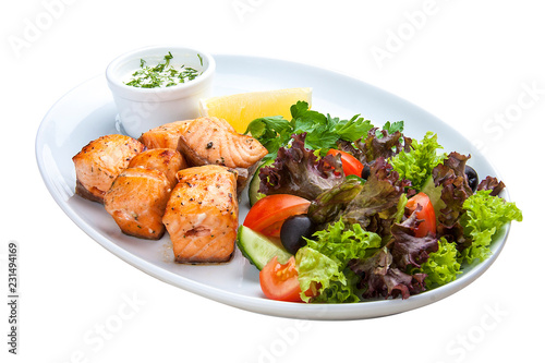 Shish kebab from salmon with vegetables and salad. On a white plate