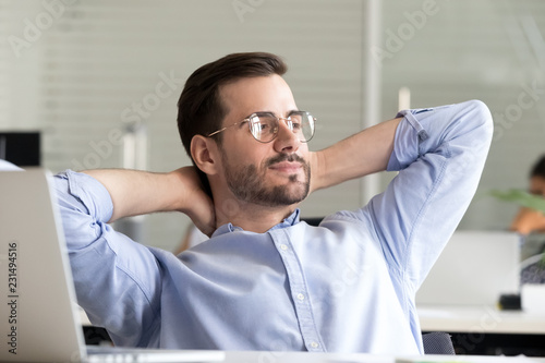 Relaxed confident business man taking break from work on laptop for mind relief holding hands behind head thinking of success enjoying rest, good result of job done in office, no stress free concept