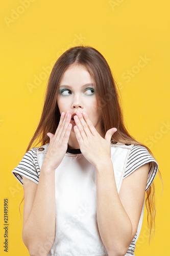 Young cute girl scaredly covers her mouth with palms