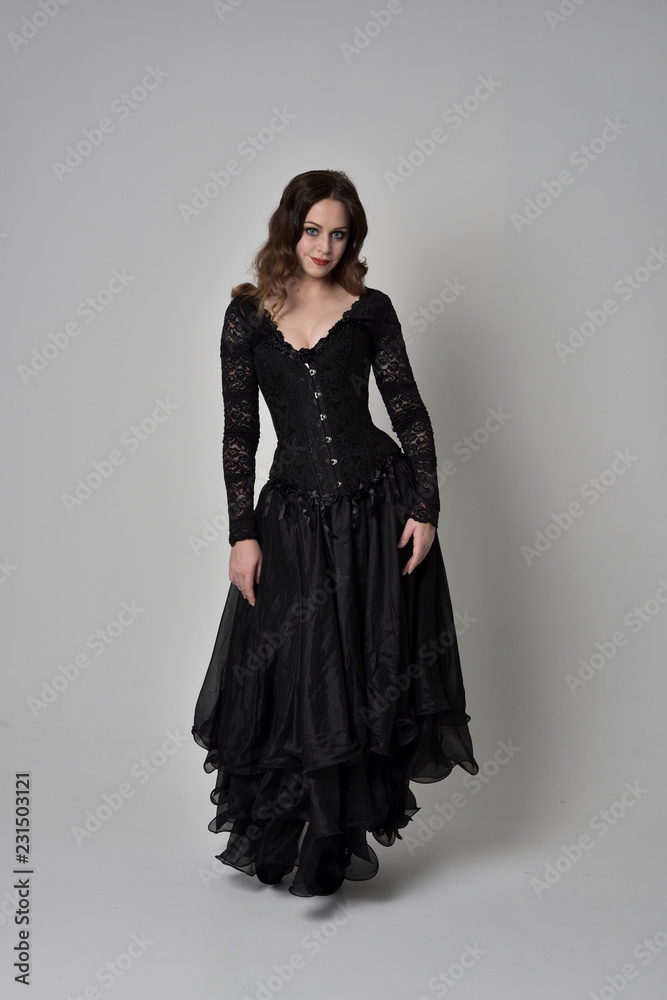 full length portrait of brunette girl wearing long black gown with corset. standing pose on grey studio background. full length portrait of brunette girl wearing long black gown with corset. standing pose on grey studio background.