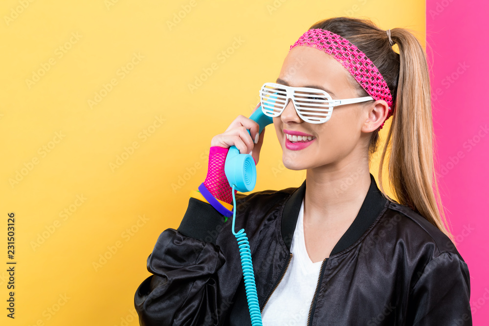 Φωτογραφία Woman in 1980's fashion with old fashioned phone on a split yellow and pink back