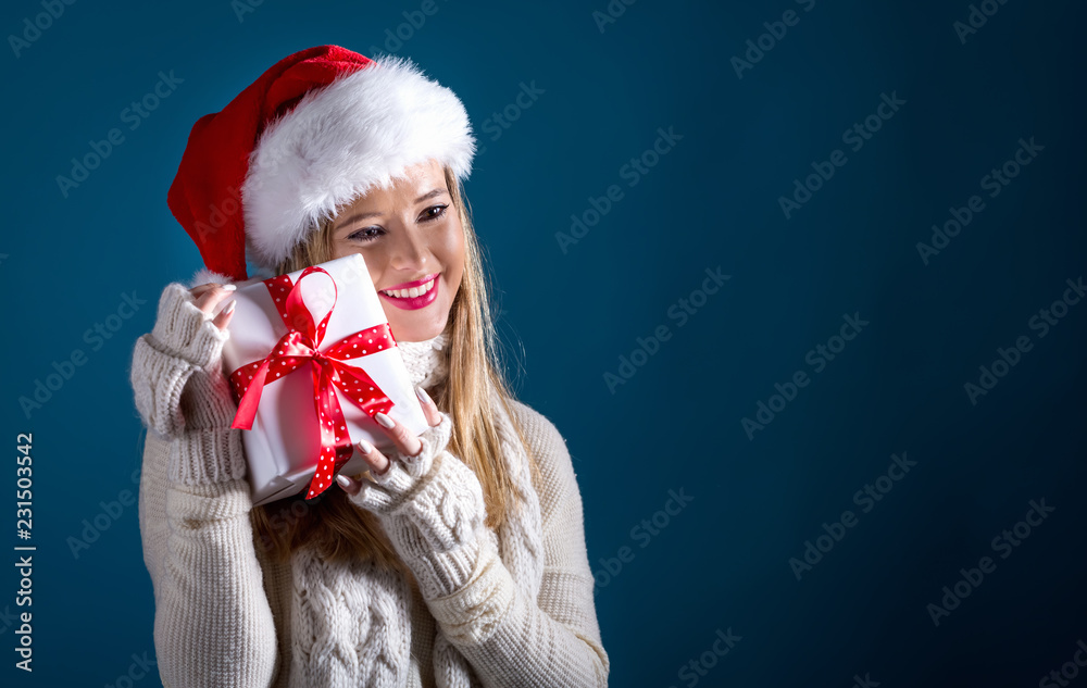 Young woman with santa hat holding a gift box on a dark blue background