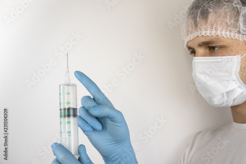 A young guy in a medical mask and hat is holding a medical syringe in front of him