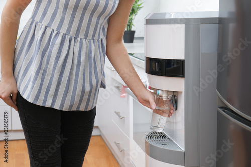 Woman filling glass from water cooler in office