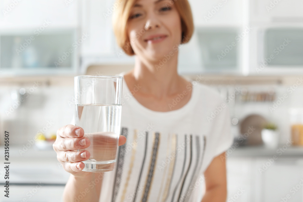 Woman holding glass with clean water in kitchen, closeup Woman holding glass with clean water in kitchen, closeup