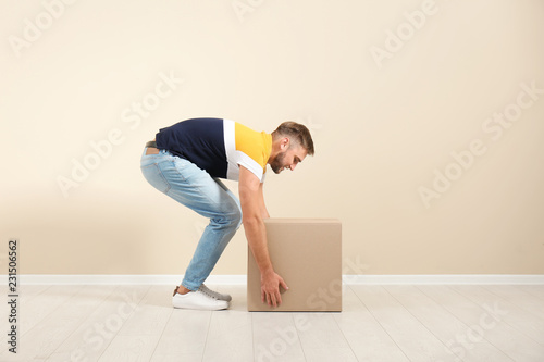 Full length portrait of young man lifting carton box near color wall. Posture concept