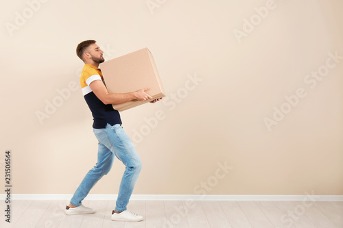 Full length portrait of young man carrying carton box near color wall. Posture concept