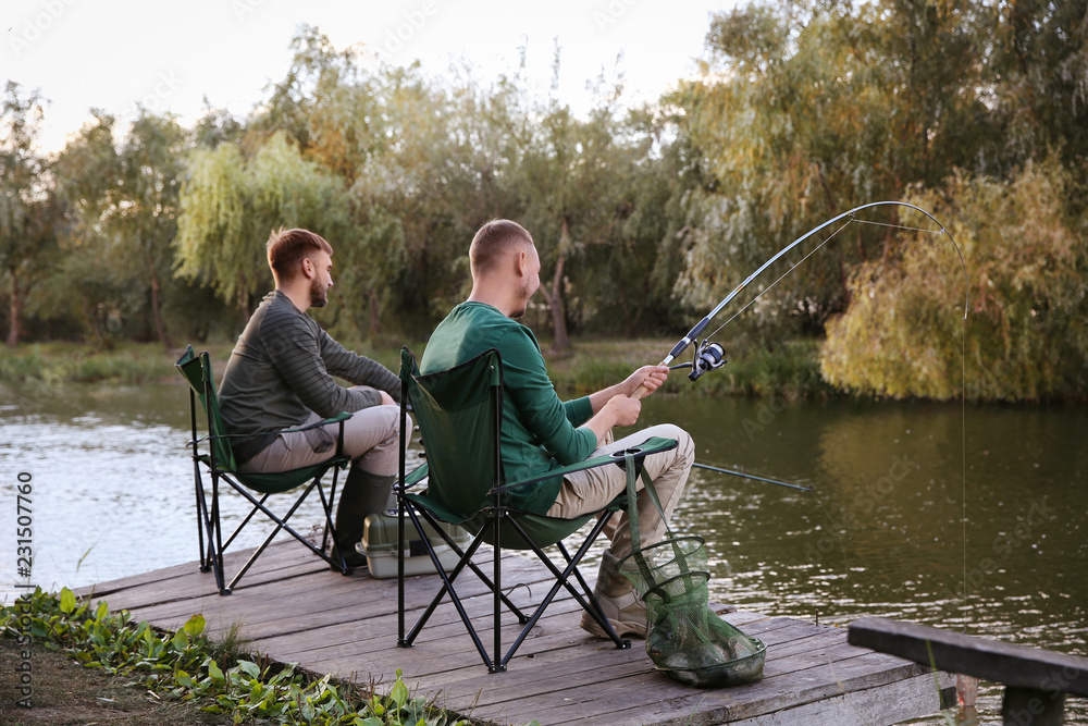 Friends fishing on wooden pier at riverside. Recreational activity Friends fishing on wooden pier at riverside. Recreational activity