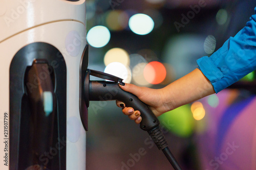 Electric vehicle charger hold by woman hand and charging on street with street charge docking station 
