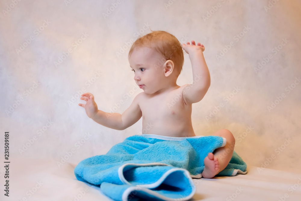 A boy in a blue towel sitting on a light background after a bath. Newborn baby resting in after bath or shower
