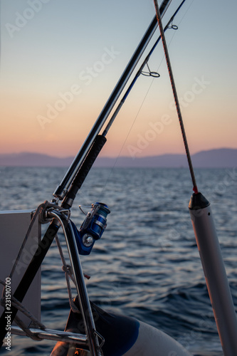 Boat fishing rods over a beautiful sunset seascape at sea around the aegean islands in greece vertical