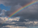 Colourful rainbow over a cloudy blue sky background. 