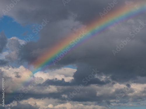 Colourful rainbow over a cloudy blue sky background.  © Gabriel