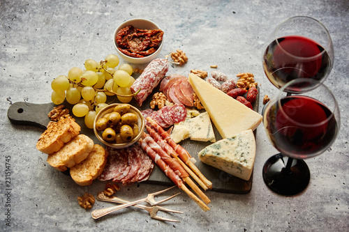 Antipasto platter cold meat and cheese board with grapes, wine, various kinds of cheese, grissini bread sticks on white rustic background. View from above