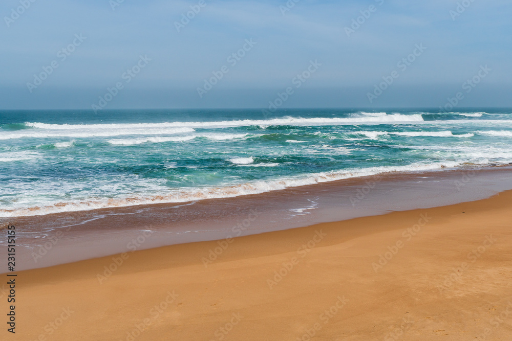 Summer day and sandy beach background. Golden sand and soft blue ocean waves on Guincho Beach (Praia da Guincho) in Cascais, Portugal. 